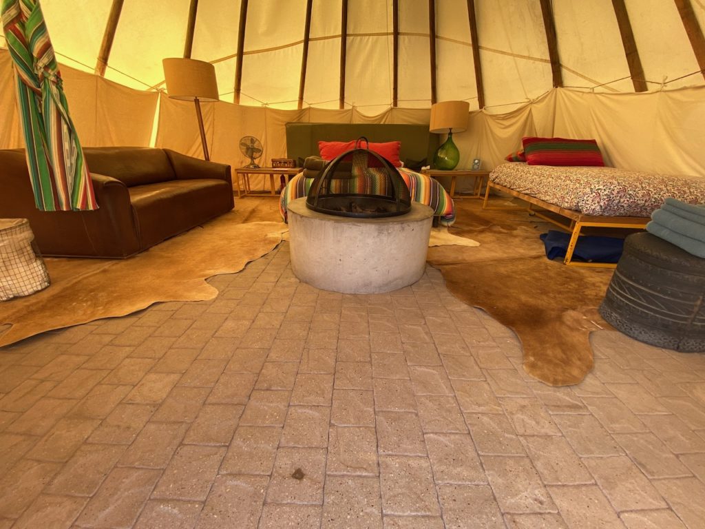 The inside of a tipi with two beds, a fire pit, and a love seat.